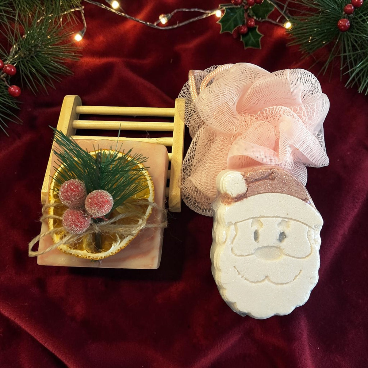 cranberry orange spa gift set featuring cranberry orange soap, santa shaped bath bomb, bamboo soap ladder and loofah on a red fabric surface 