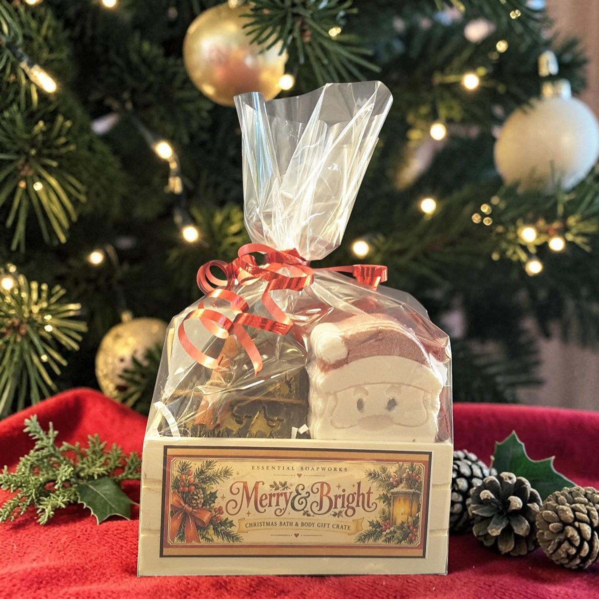 winter solstice christmas gift crate spa set featuring winter solstice soap, santa shaped bath bomb, bamboo soap ladder and loofah gift wrapped in a wooden crate on a red fabric surface with a christmas tree in the background