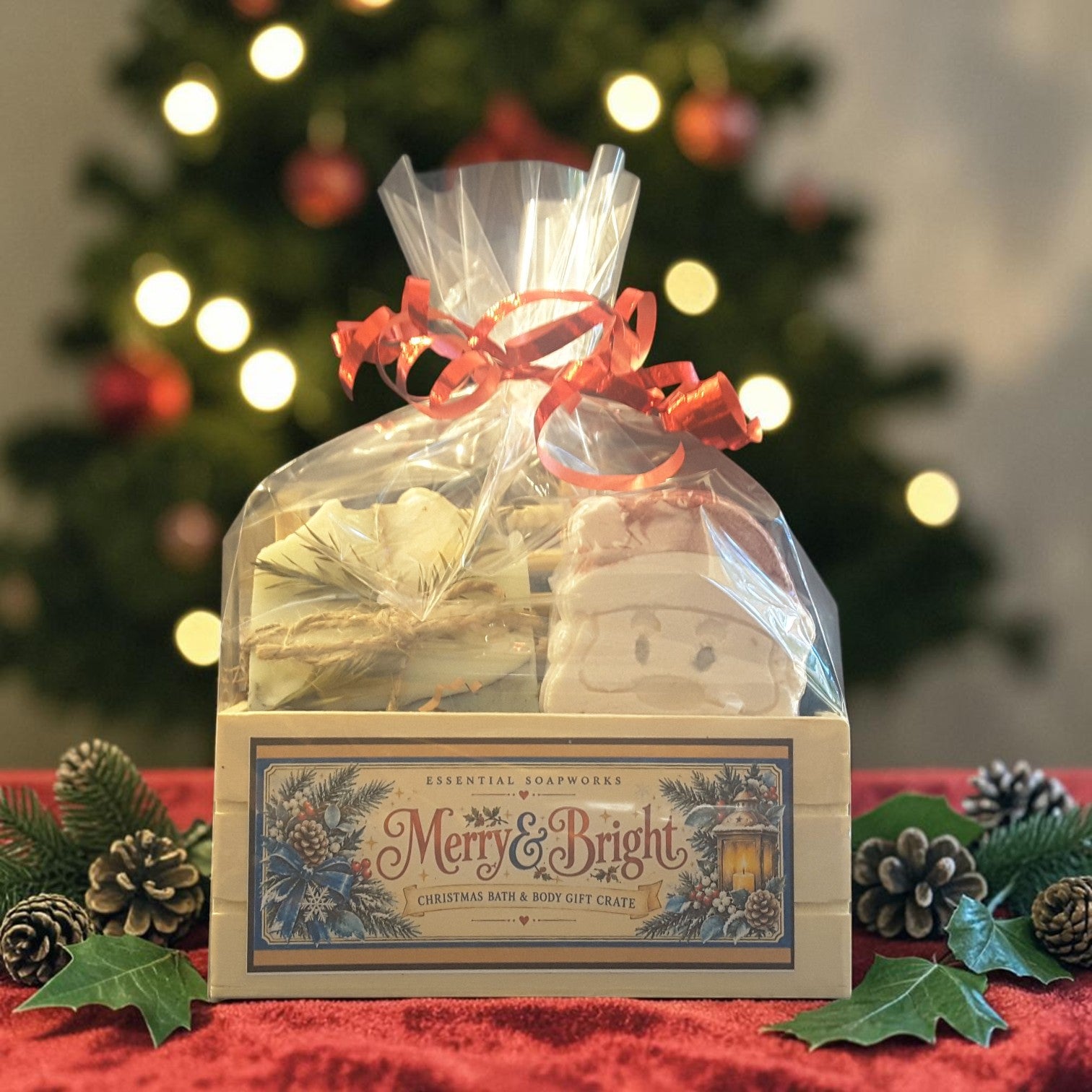 eucalyptus mint christmas gift crate spa kit featuring eucalyptus mint soap, santa shaped bath bomb, bamboo soap ladder and loofah gift wrapped in a wooden crate on a red fabric surface with a christmas tree in the background