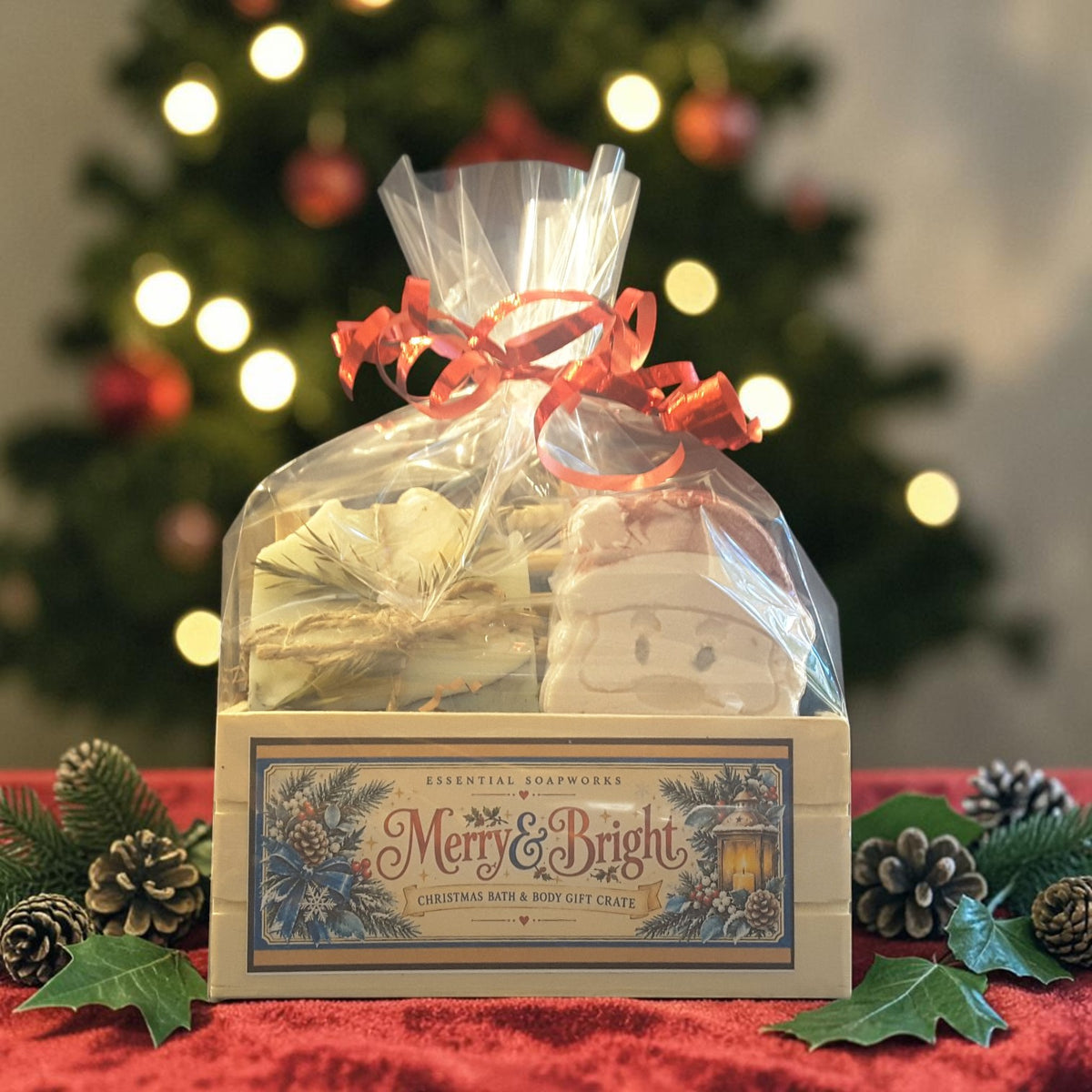 eucalyptus mint christmas gift crate spa kit featuring eucalyptus mint soap, santa shaped bath bomb, bamboo soap ladder and loofah gift wrapped in a wooden crate on a red fabric surface with a christmas tree in the background