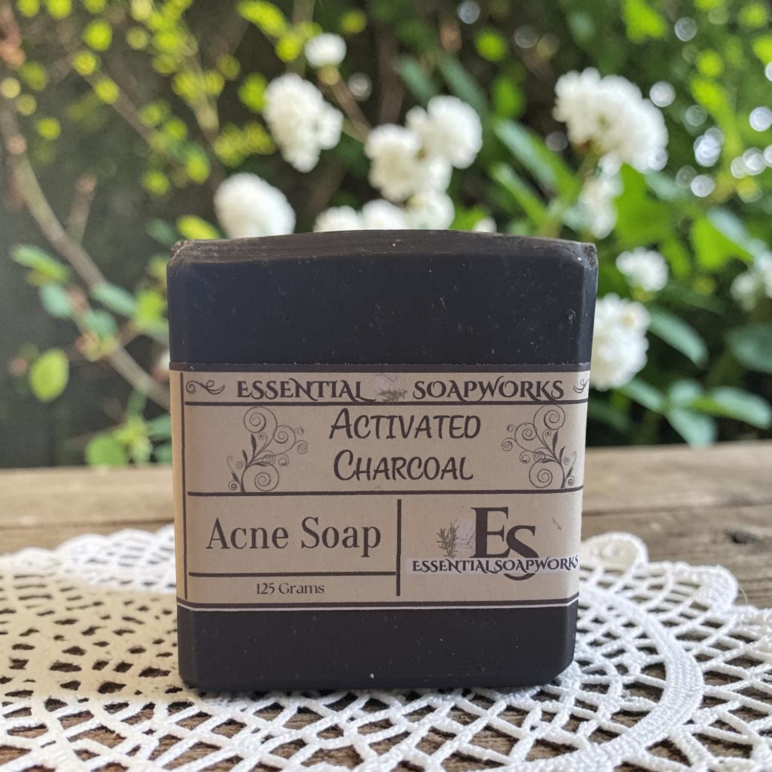 activated charcoal acne soap on a doily on a wooden surface with white flowers