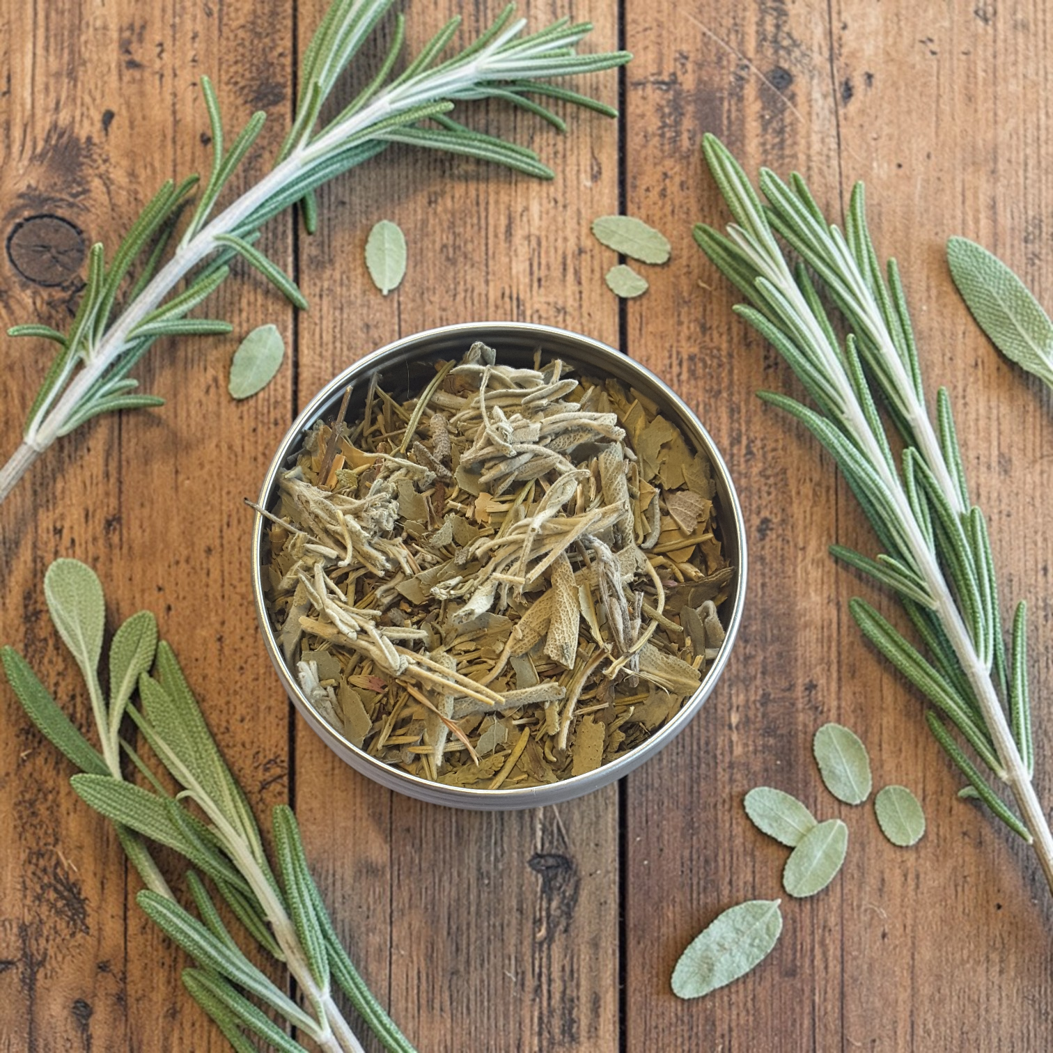 Energy Cleanse loose incense in a metal container surrounded by fresh rosemary on a wooden surface
