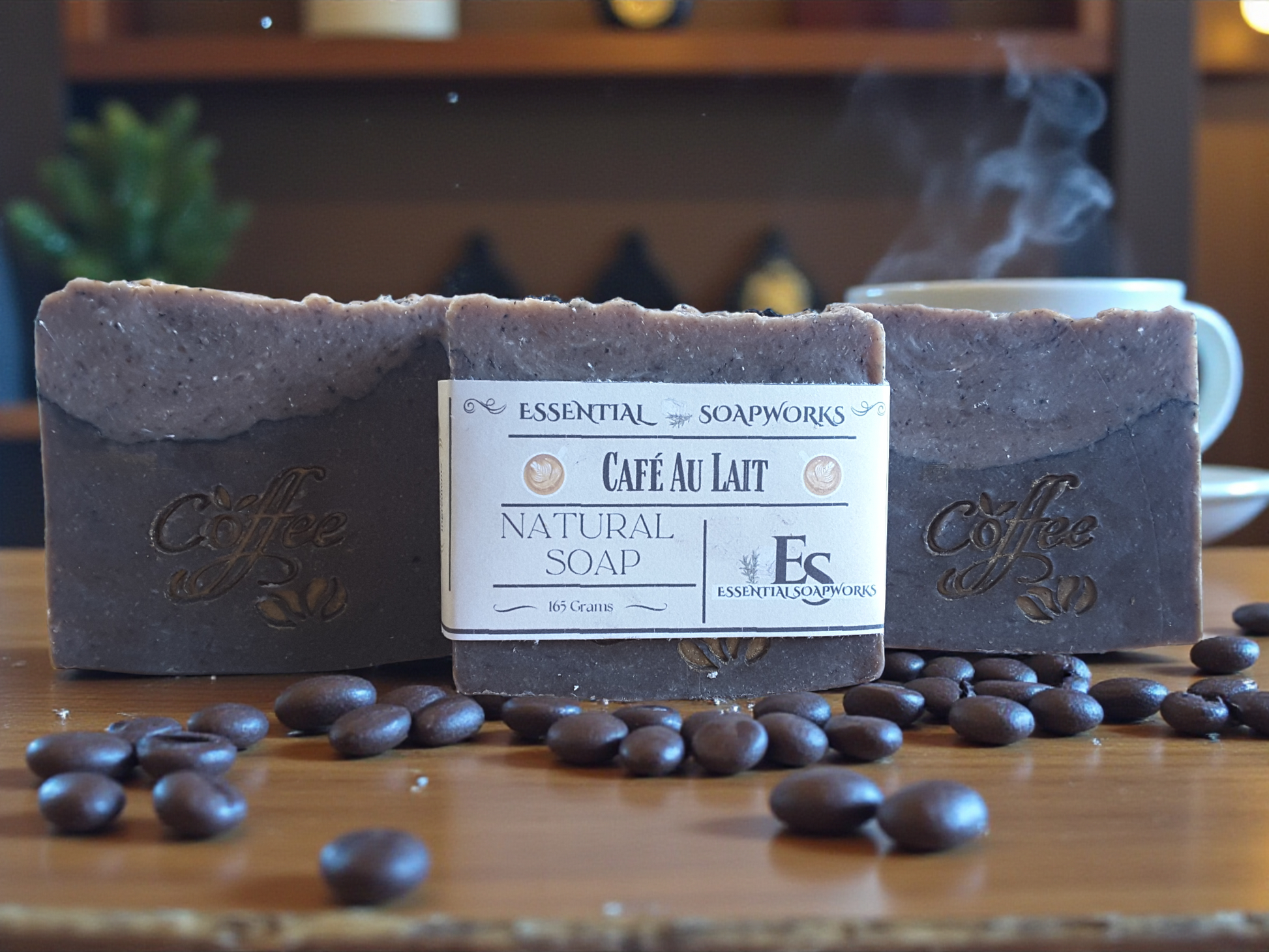 Two bars of coffee soap with a label in front of coffee beans on a wooden surface.