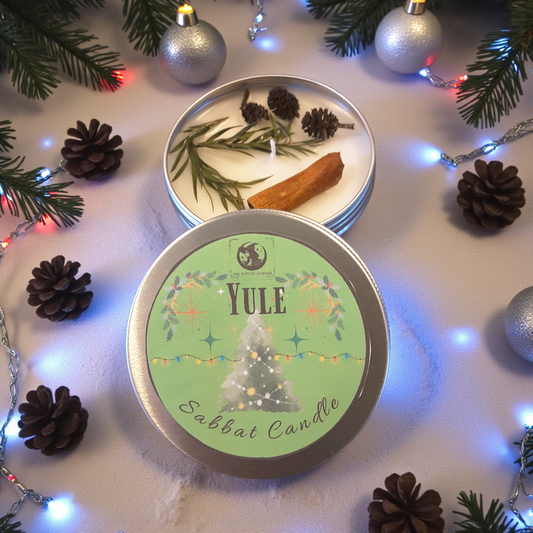 Yule candle in a tin surrounded by Christmas decorations on a white surface.