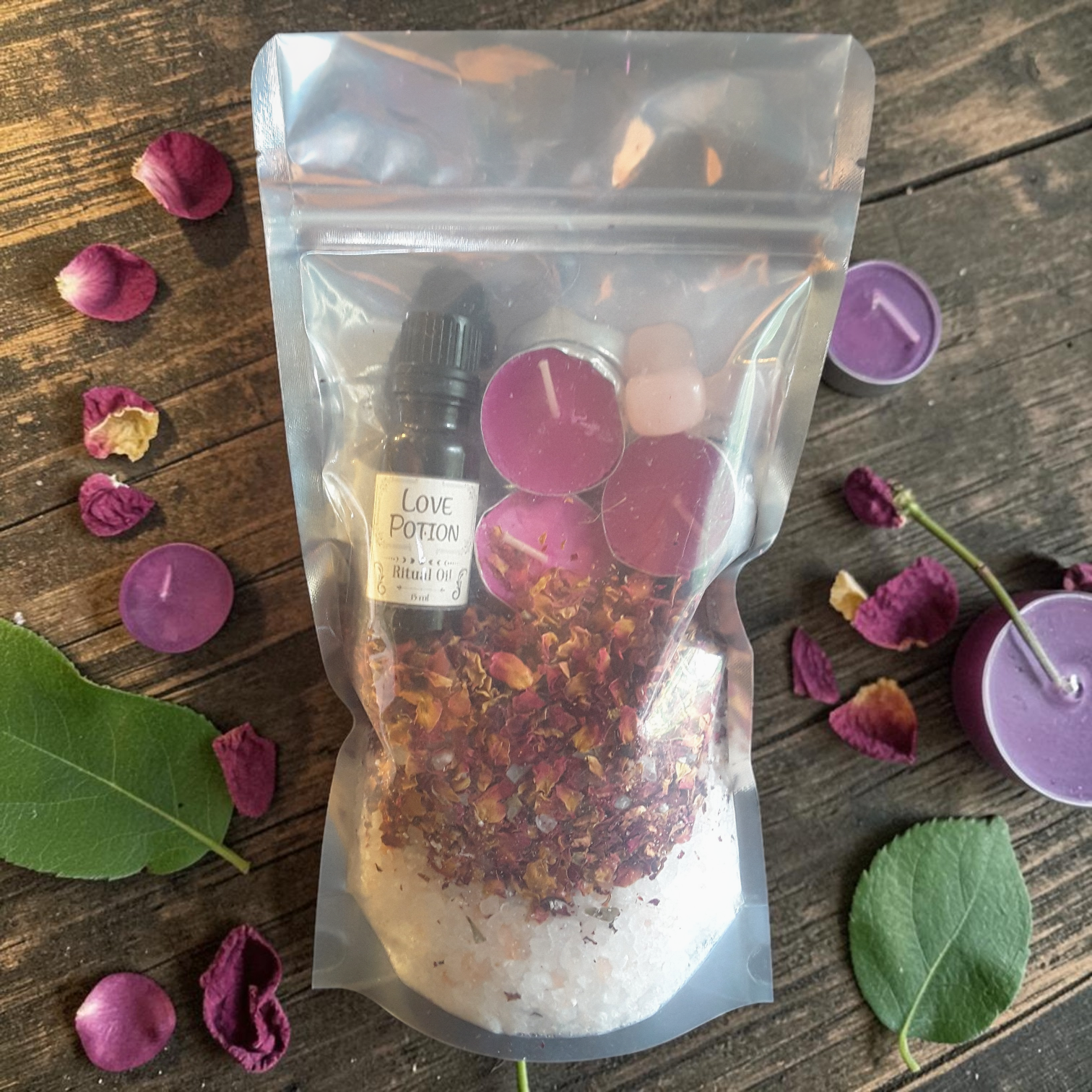 Love Spell Bath Ritual Kit with bath salts, rose petals, ritual oil, tealight candles and rose quartz crystal on a wooden surface