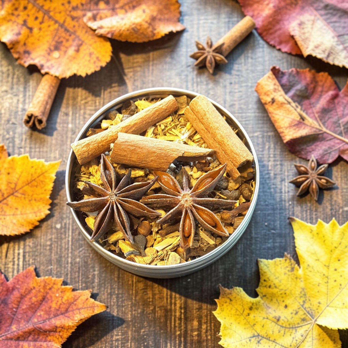 A round metal tin filled with Mabon loose incense made with warm autumn spices, including cinnamon sticks, star anise, and dried botanicals, styled on a wooden surface with scattered orange, yellow, and red leaves.