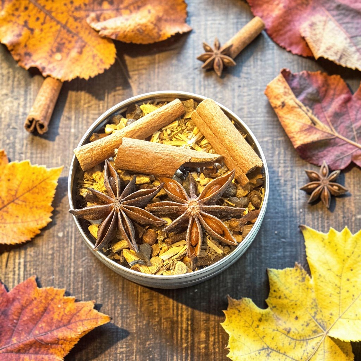A round metal tin filled with Mabon loose incense made with warm autumn spices, including cinnamon sticks, star anise, and dried botanicals, styled on a wooden surface with scattered orange, yellow, and red leaves.