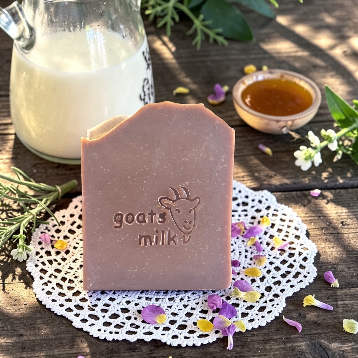 Bar of goats milk soap on a doily with a jar of milk and honeycomb in the background.