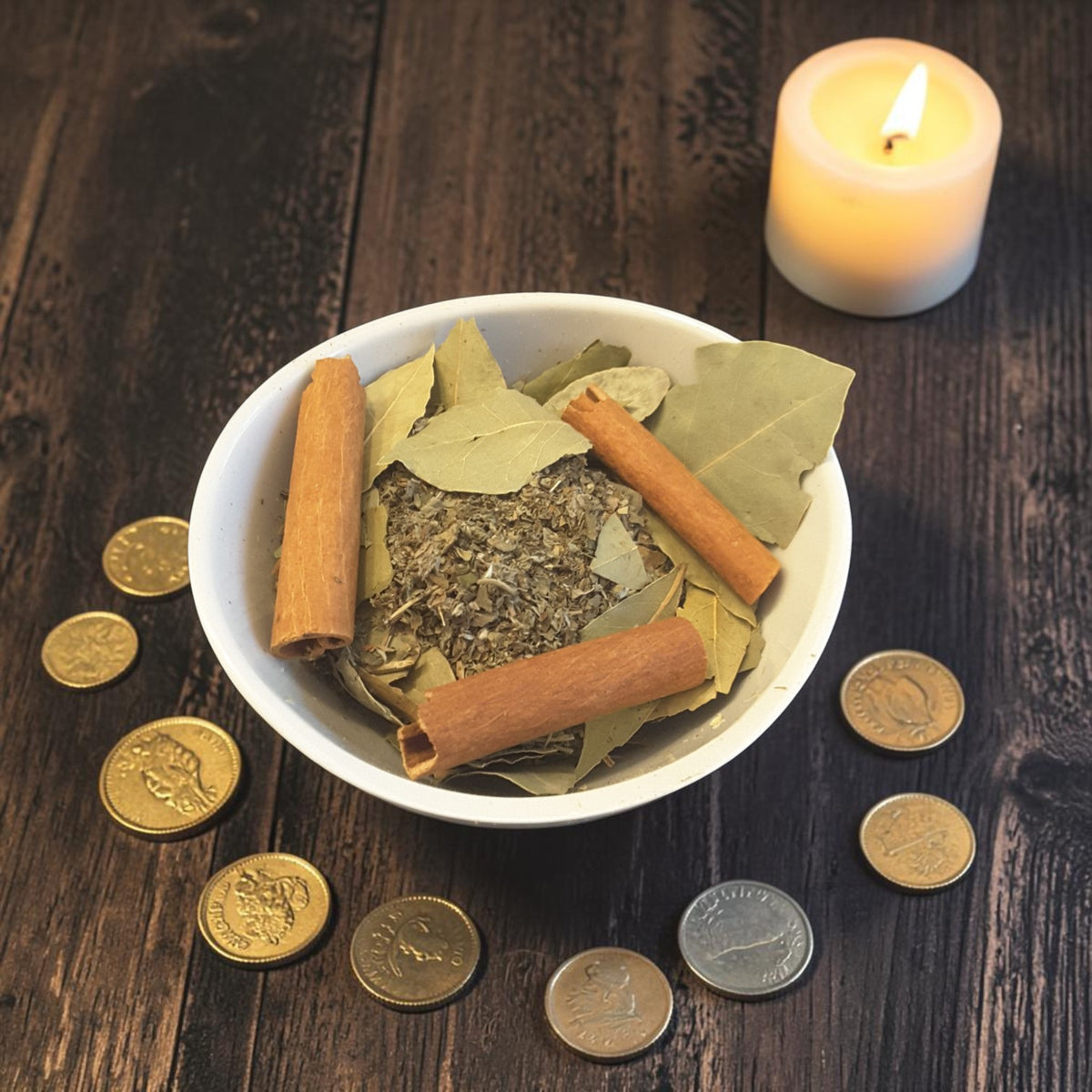 a bowl of abundance tub tea on a dark wooden surface with gold coins, bay leaves, cinnamon sticks and candles