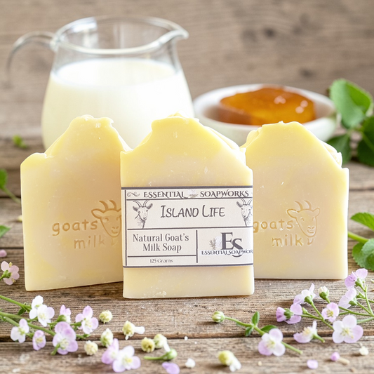 Three goat milk soap bars surrounded by flowers on a wooden surface.