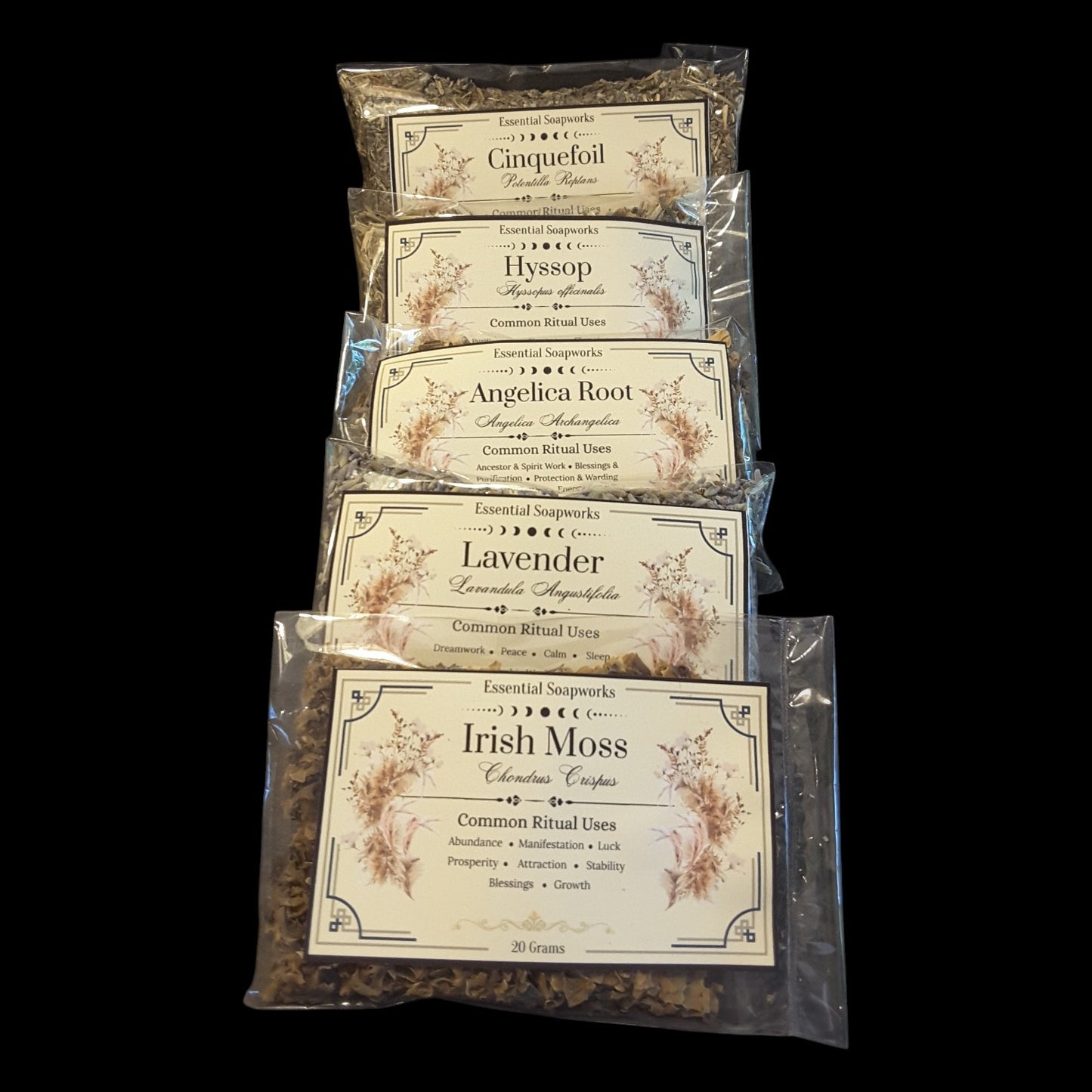 Five clear plastic bags of dried herbs for witchcraft arranged in a vertical stack on a solid black background. The labels show different herbs: Cinquefoil, Hyssop, Angelica Root, Lavender, and Irish Moss.