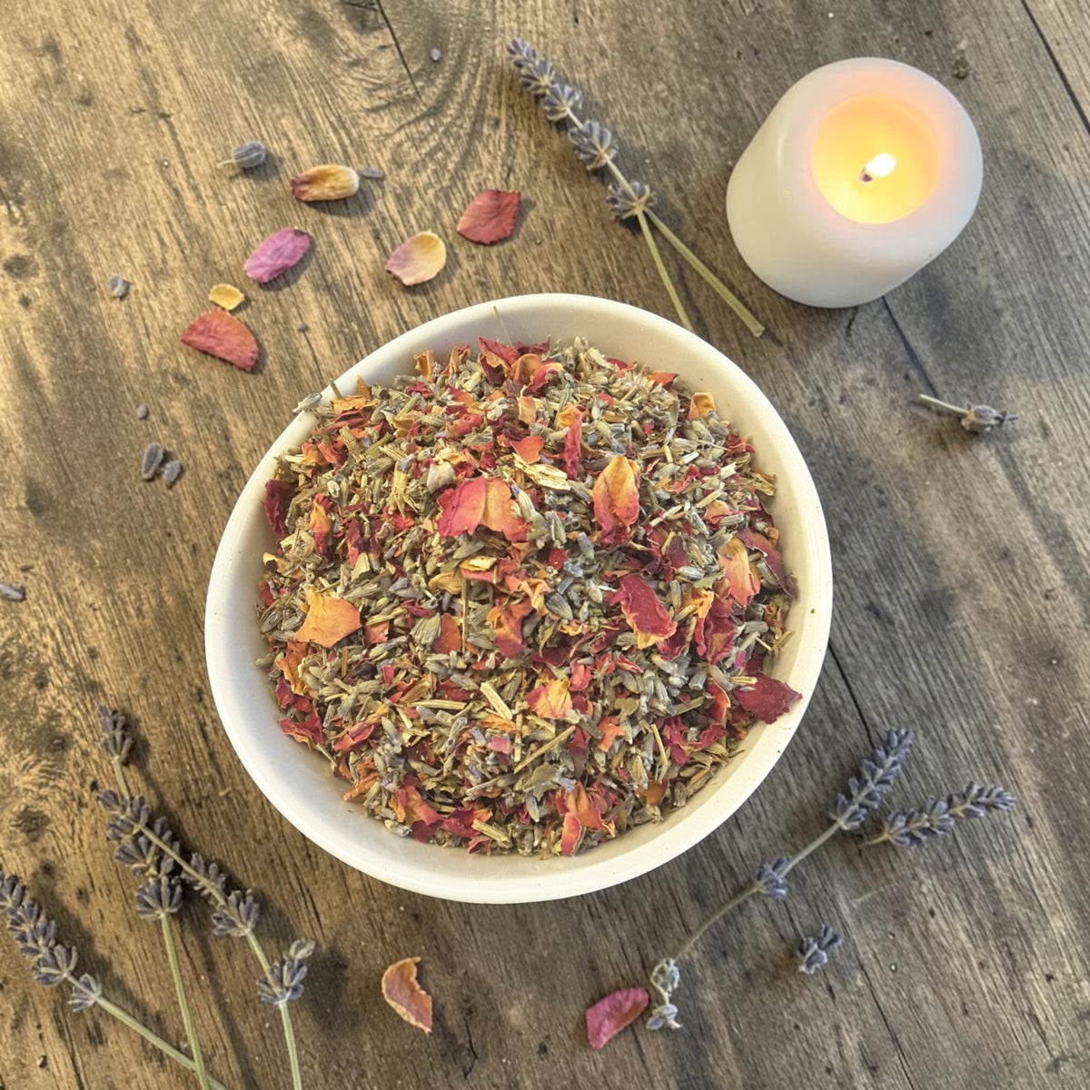 a bowl of blessings tub tea on a dark wooden surface with rose petals, lavender and candles