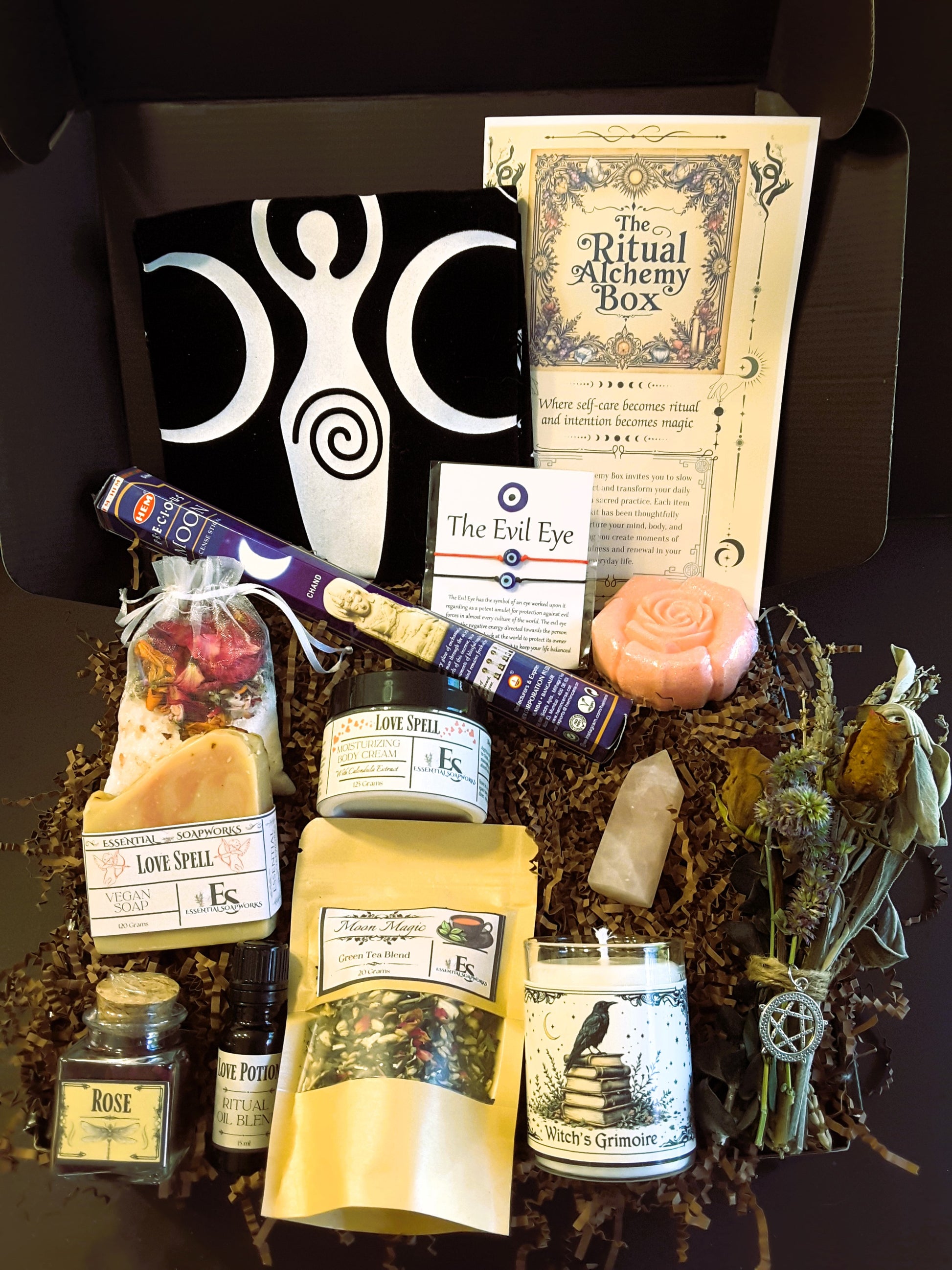 Witchy subscription box with various items including a candle, herbs, and packaging on a dark surface.