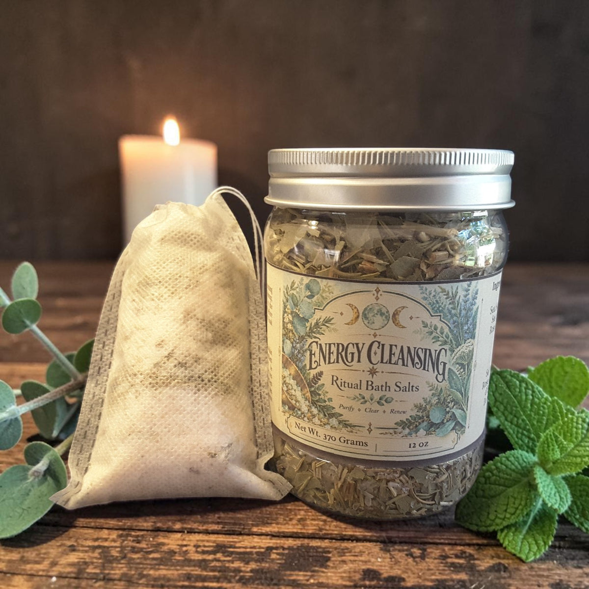 energy cleansing bath salts in a jar on a dark wooden surface next to a muslin bag filled with bath salts alongside mint leaves and candles