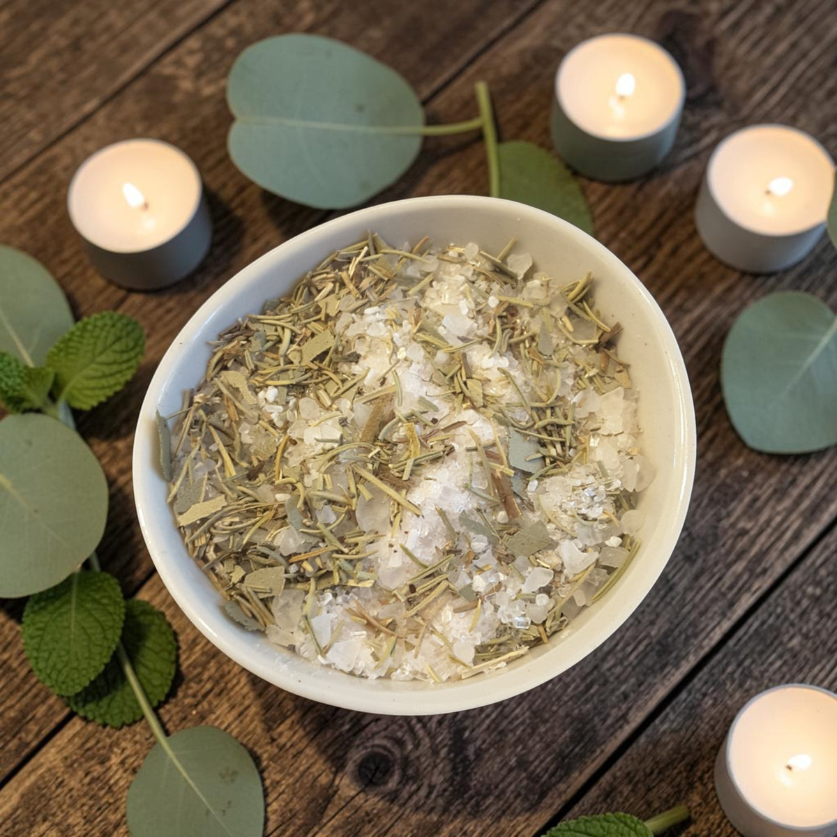 a bowl of energy cleansing bath salts on a dark wooden surface with mint leaves and candles