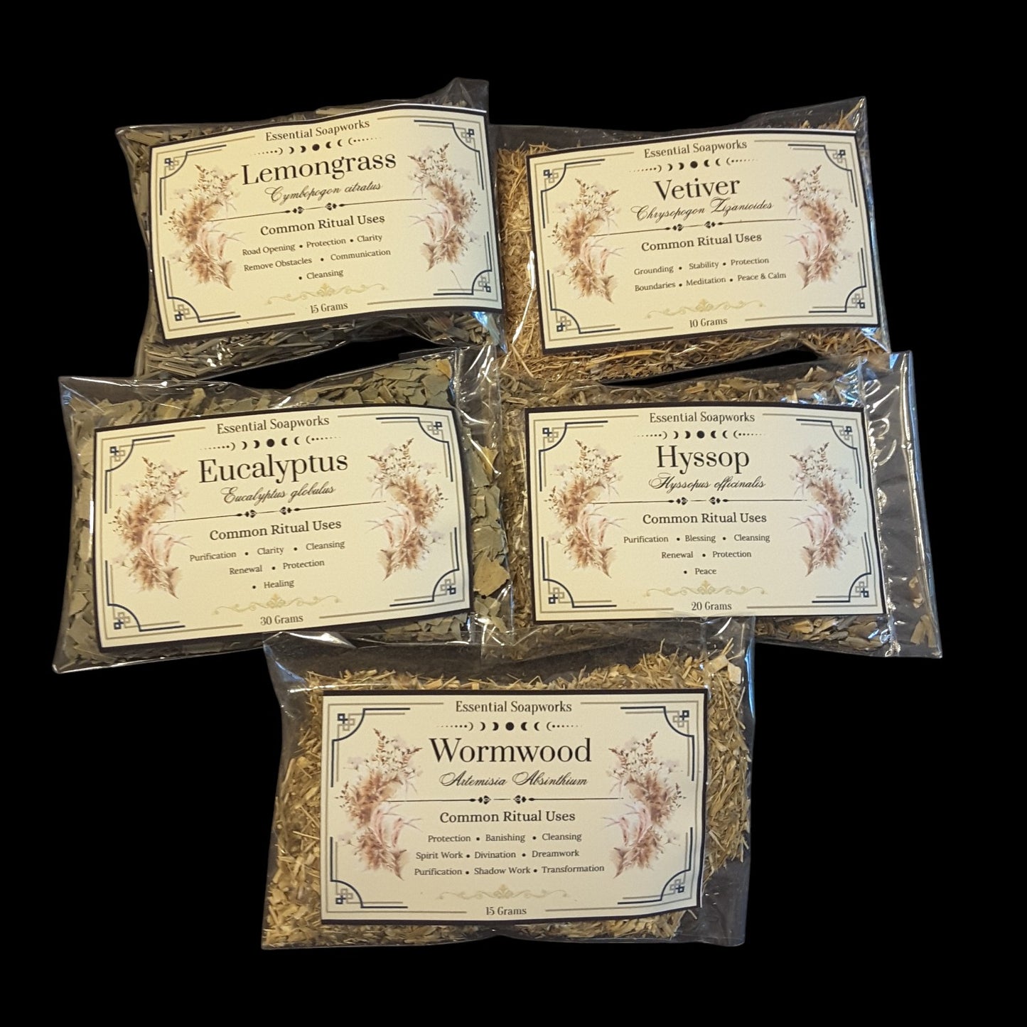 Five clear plastic bags of energy cleansing herbs for witchcraft with cream-colored labels are arranged on a solid black background. The labels feature botanical illustrations and names of the herbs: Lemongrass, Vetiver, Eucalyptus, Hyssop, and Wormwood.