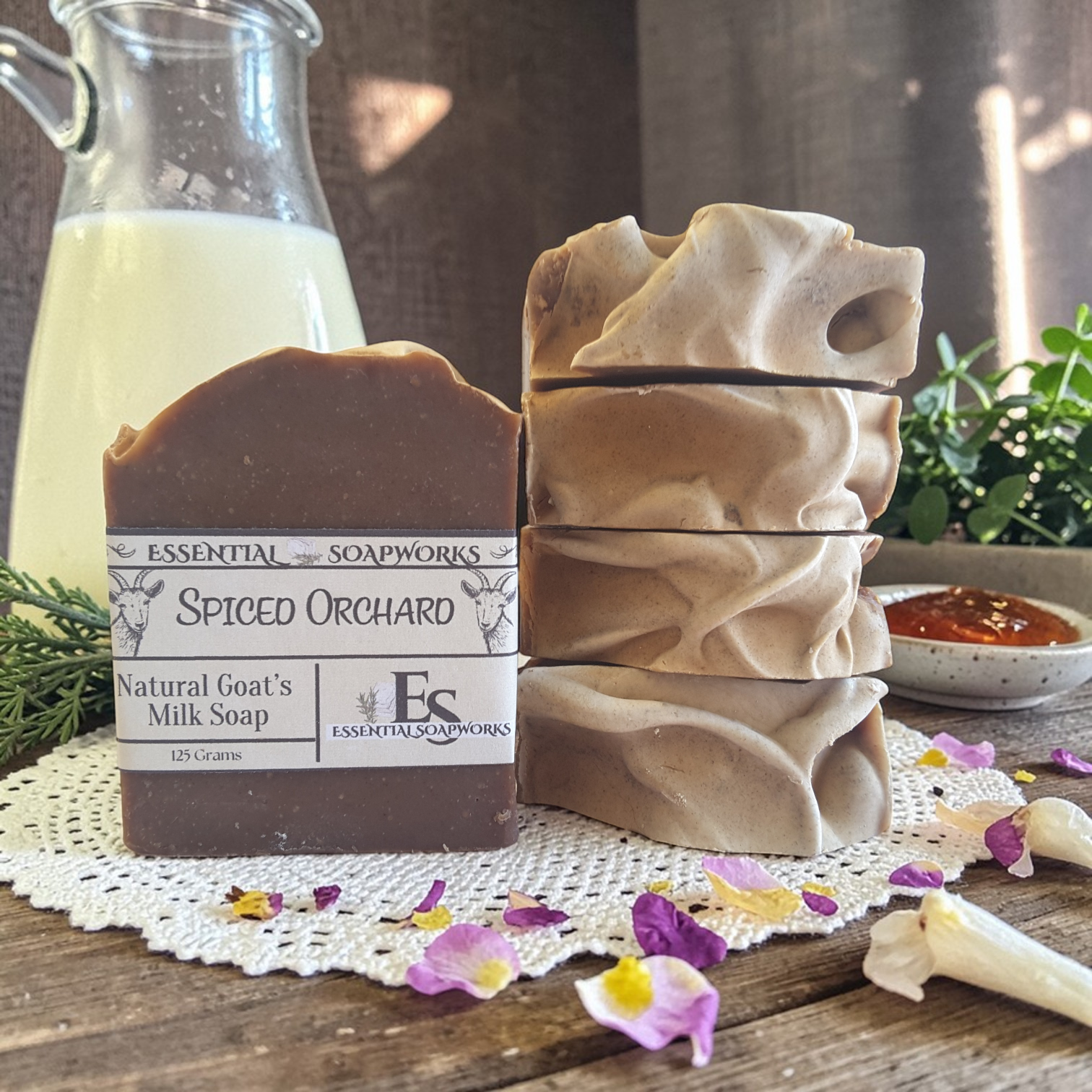 goat milk soap bars with a decorative label on a wooden surface with flowers and a glass container.