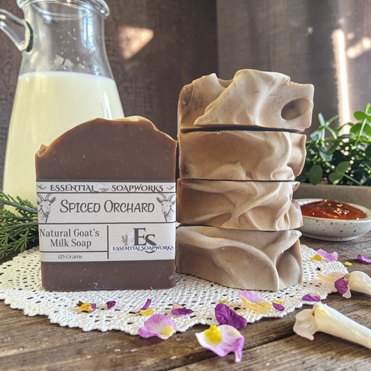 goat milk soap bars with a decorative label on a wooden surface with flowers and a glass container.