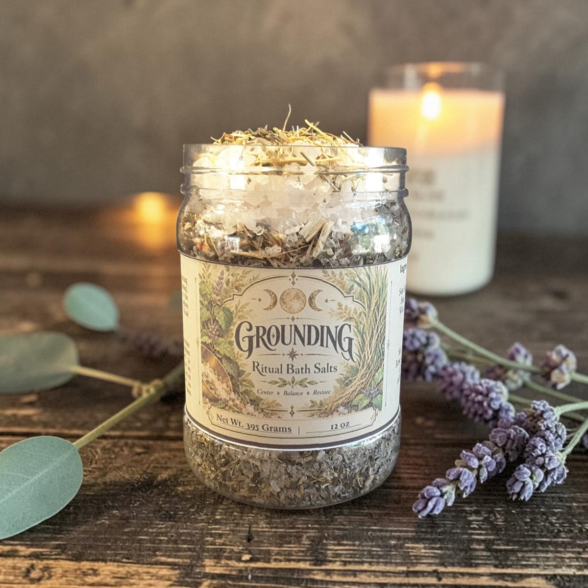 grounding bath salts in a jar on a dark wooden surface with candles and greenery in the background