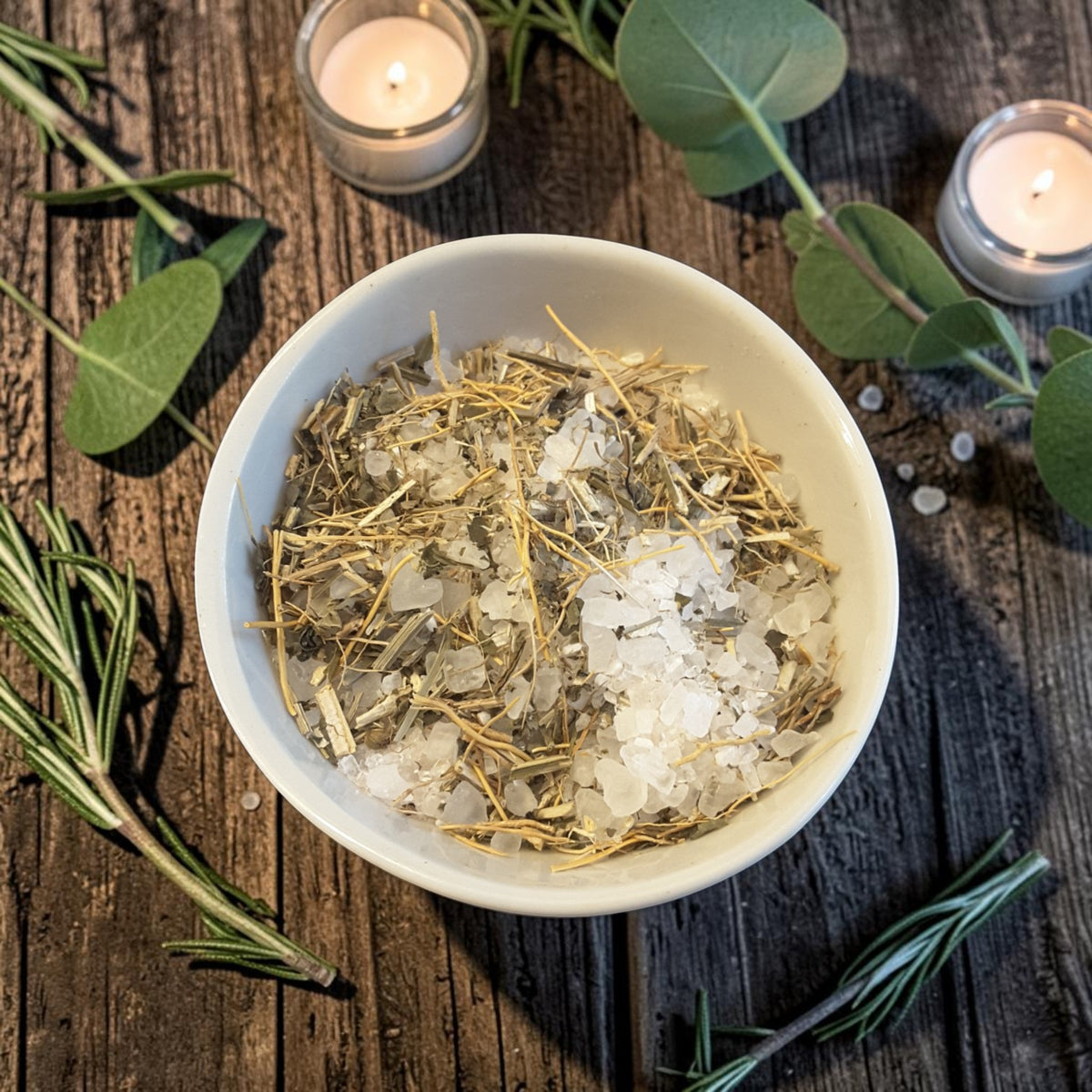 grounding bath salts in a bowl on a dark wooden surface with candles and greenery 