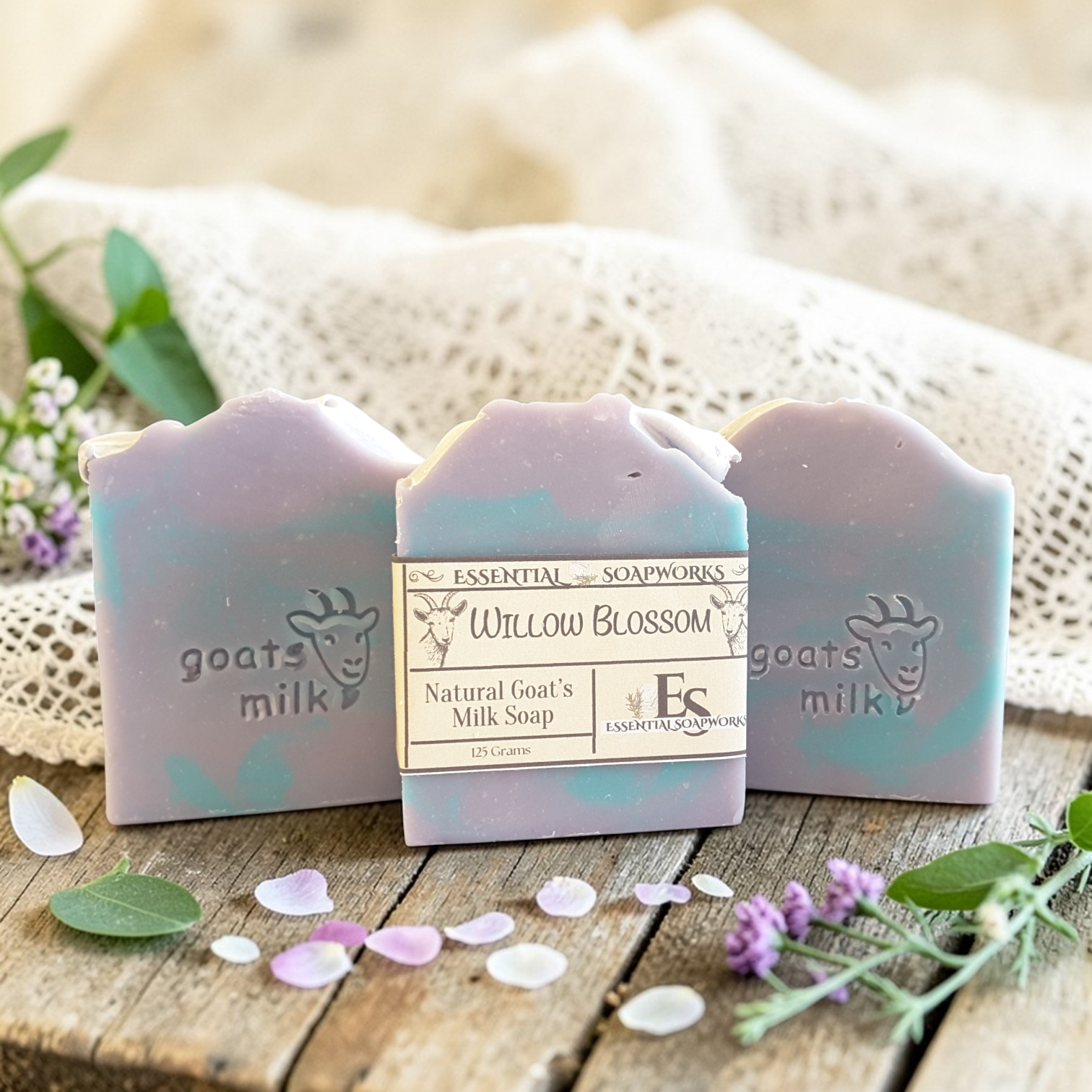 Natural goat milk soap bars on a wooden surface with flowers and leaves