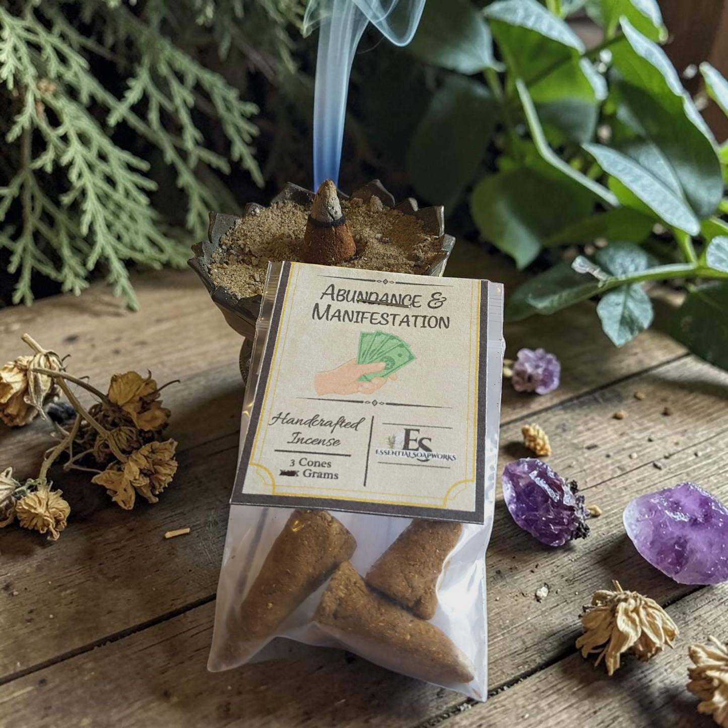 Incense cones labeled 'Abundance & Manifestation' with smoke, plants, and crystals on a wooden surface.