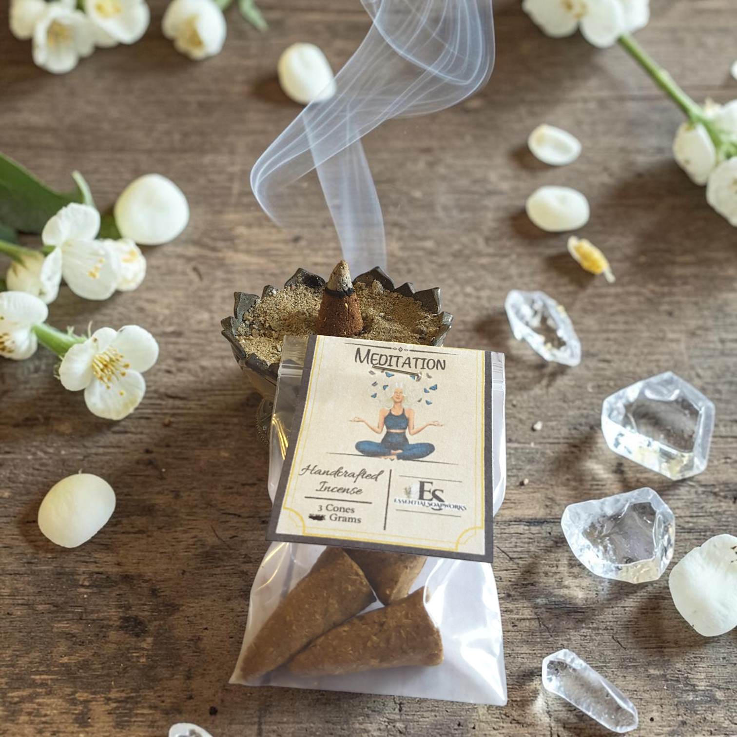 Meditation incense cones with smoke on a wooden surface with flowers and crystals.