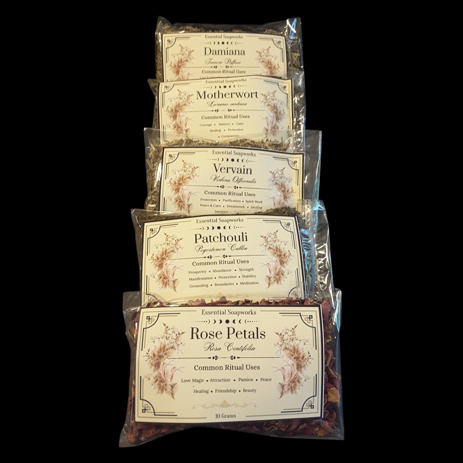 Five clear plastic bags of witchy herbs for love spells and rituals stacked vertically on a black background. The labels read Daminia, Motherwort, Vervain, Patchouli, and Rose Petals, with floral illustrations and common ritual uses printed on the cream-colored labels.
