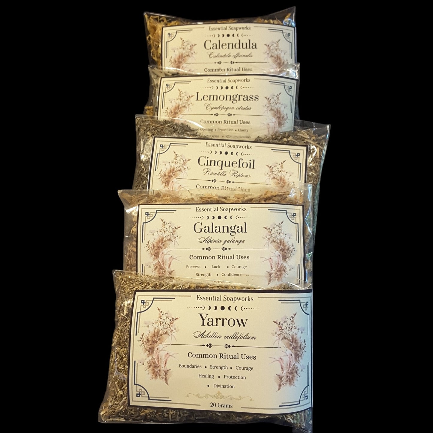 Five clear plastic bags of witchy herbs for success and personal power stacked vertically against a solid black background. They are labeled with different herbs: Calendula, Lemongrass, cinquefoil, Galangal, and Yarrow.