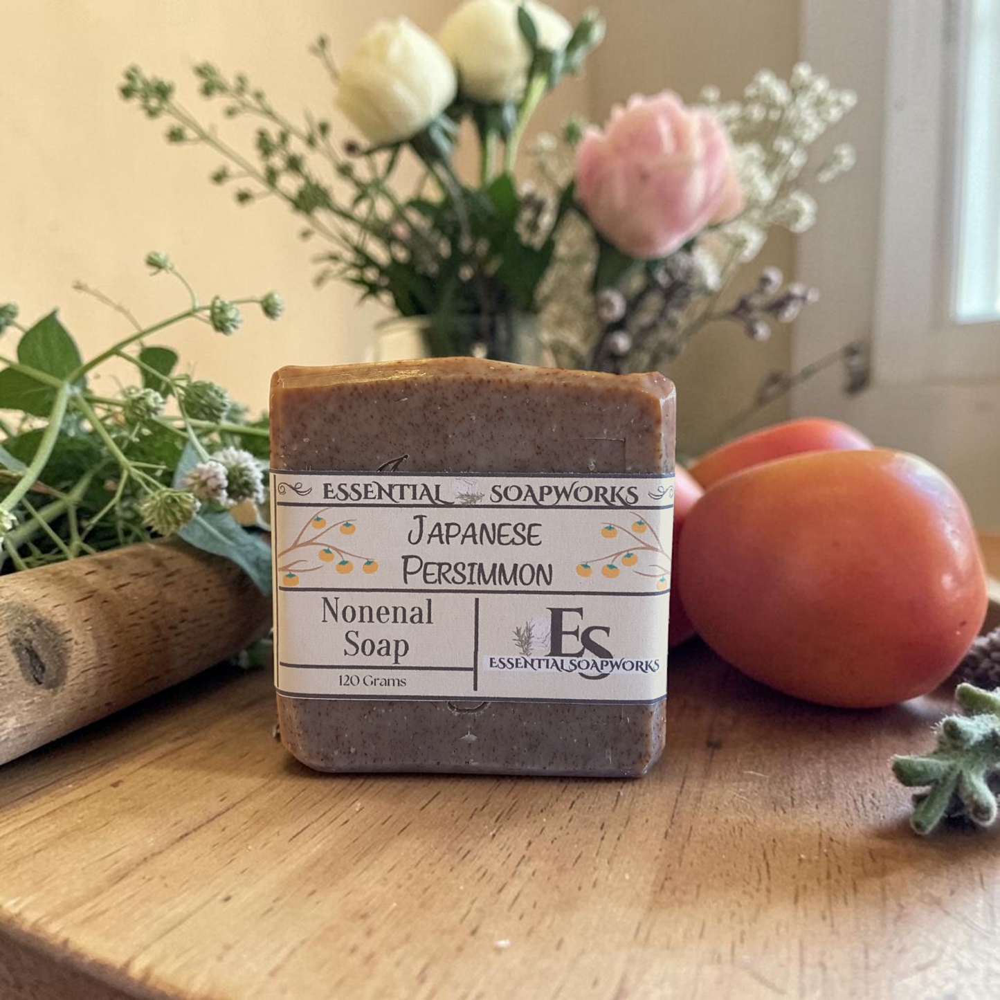 Persimmon Soap - Nonenal Soap on a wooden surface with flowers and peaches in the background