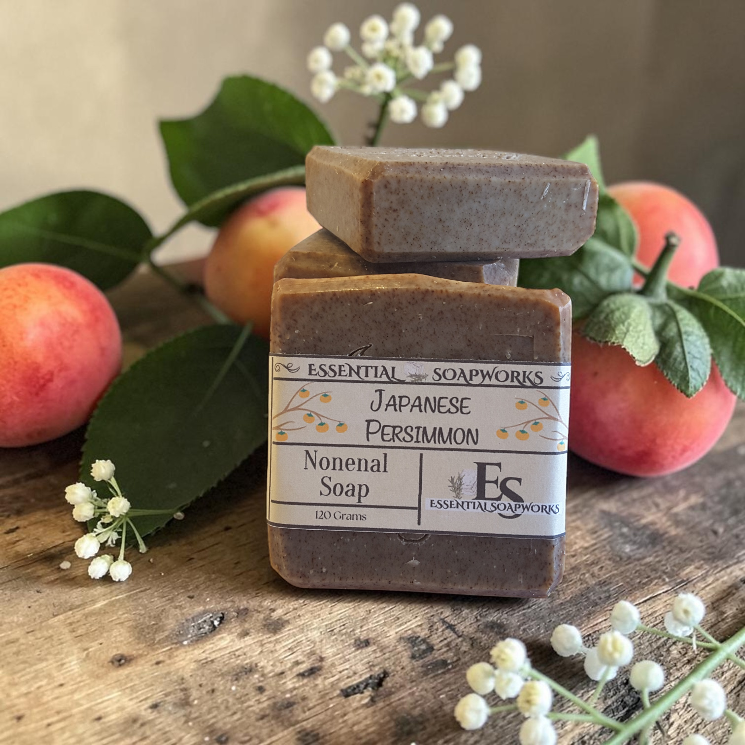 Japanese Persimmon Nonenal Soap from Essential Soapworks on a wooden surface with persimmons and leaves.