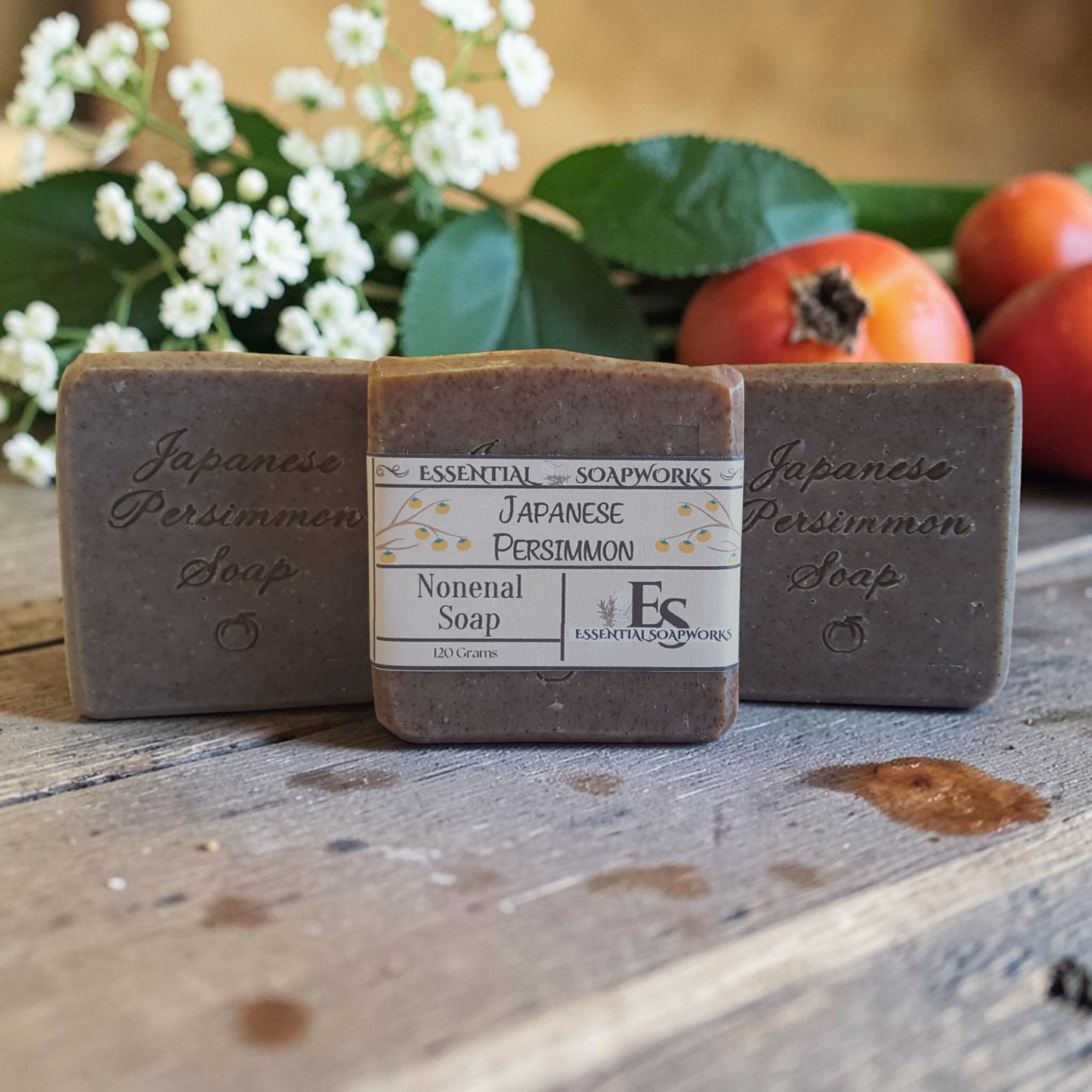Three bars of Japanese Persimmon soap on a wooden surface with flowers and persimmons in the background.