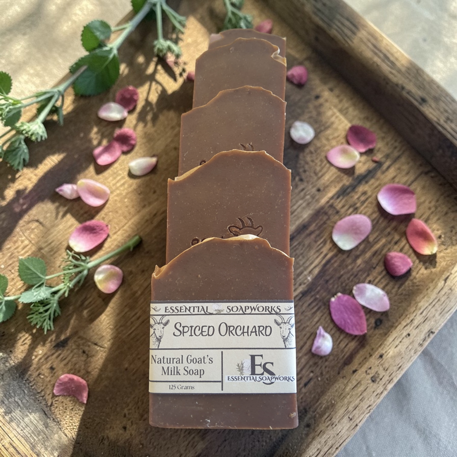 goat milk soap bars on a wooden surface with flowers and leaves.