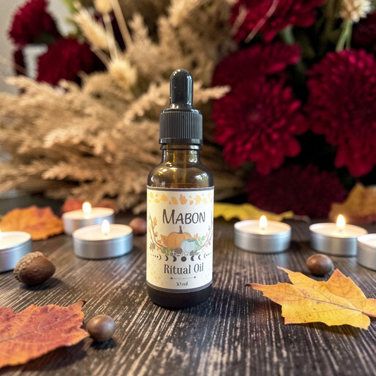 Mabon ritual oil on a wooden surface with fall leaves and tealight candles with fall flowers in the background