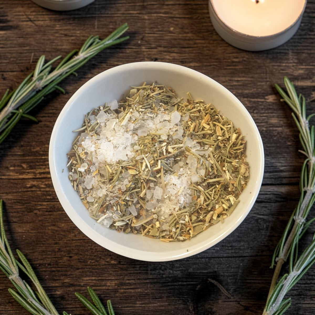 a bowl of protection herbal bath salts on a dark wooden surface with rosemary and candles