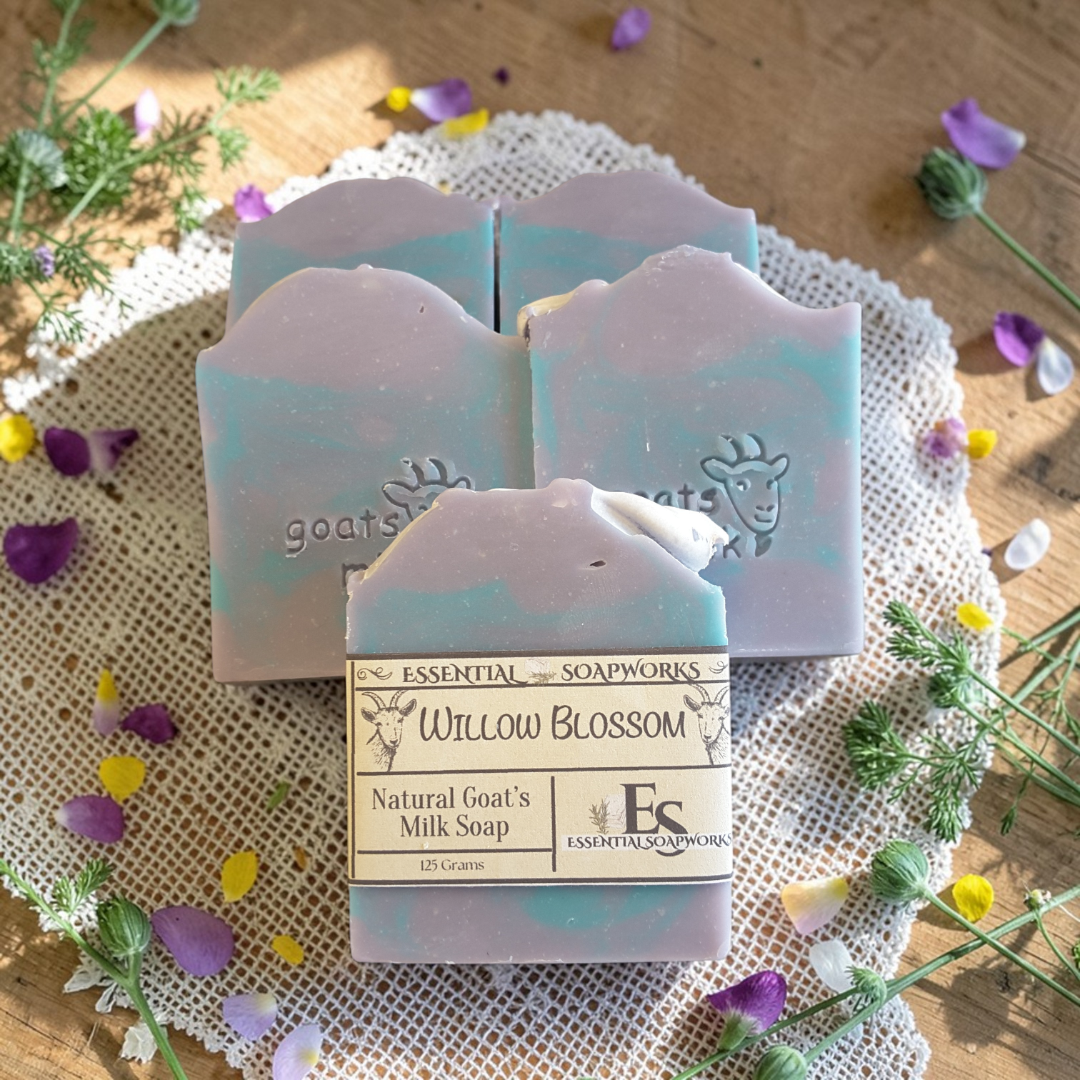 Goat's milk soap bars with packaging on a wooden surface with flowers