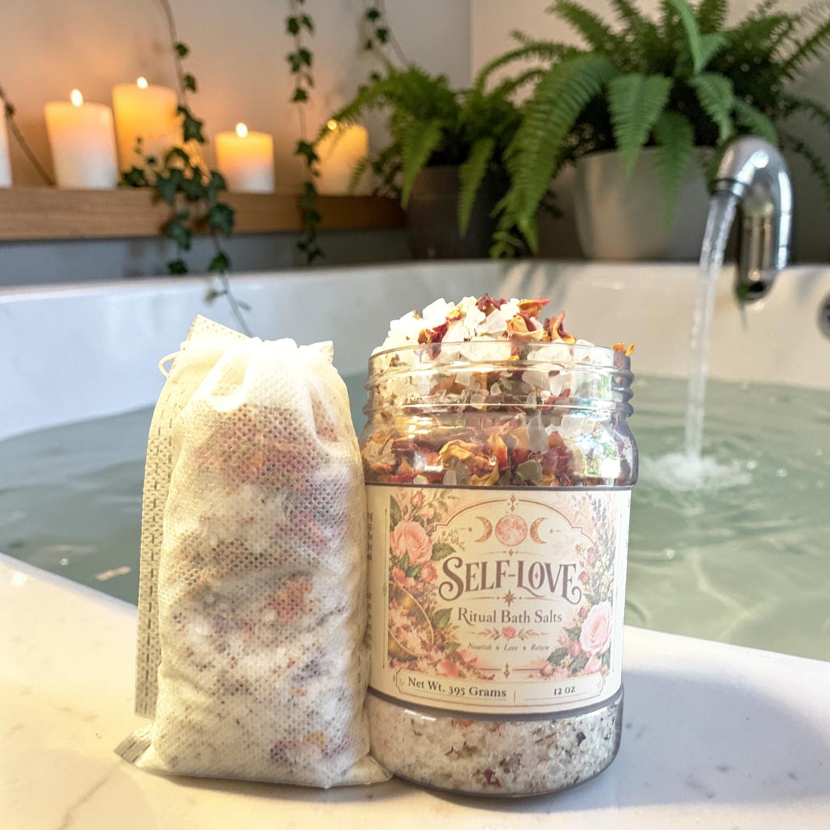 self-love bath salts in a jar next to a muslin bag filled with bath salts on the edge of a bathtub with plants and candles in the background