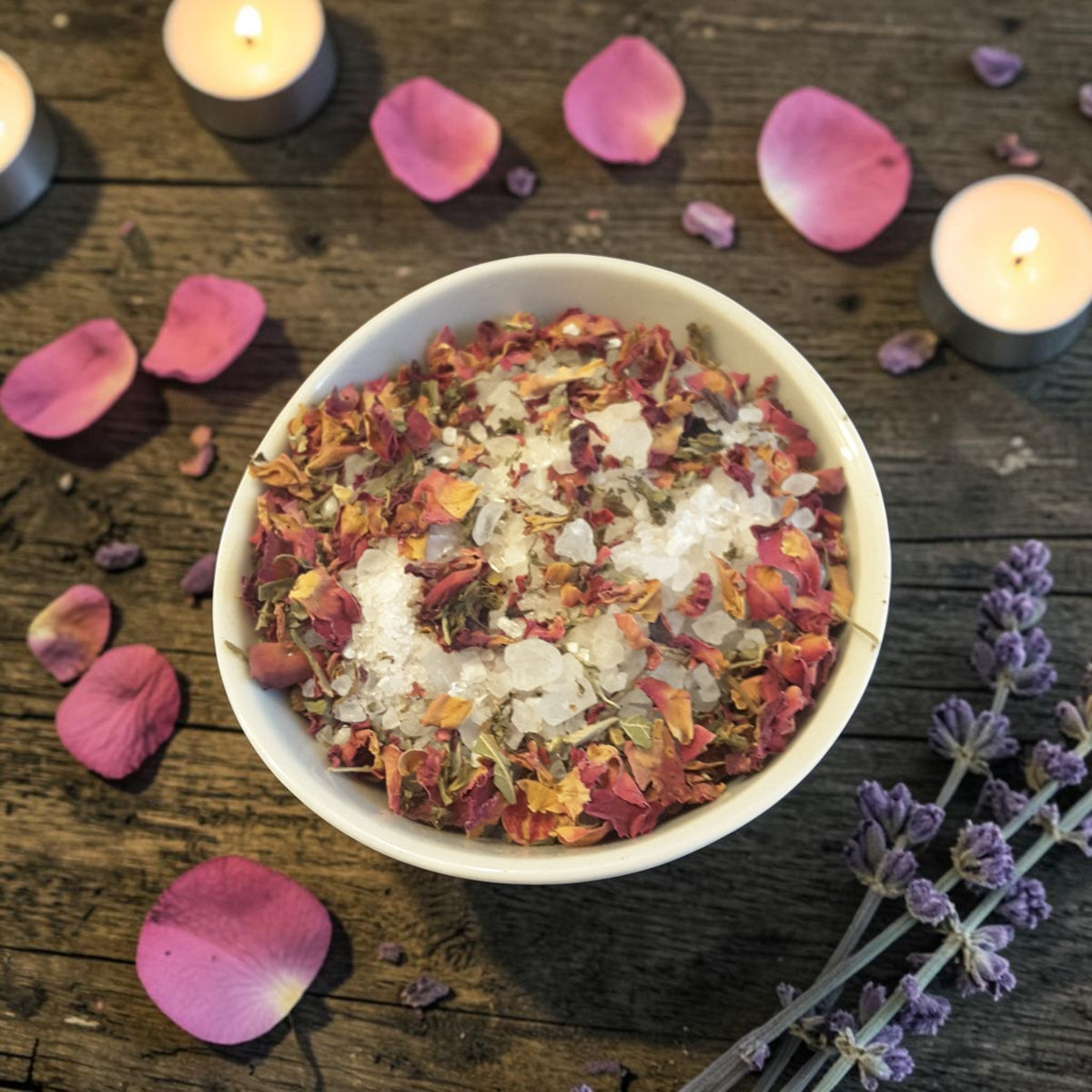a bowl of self-love bath salts on a wooden surface with lavender, roses and candles