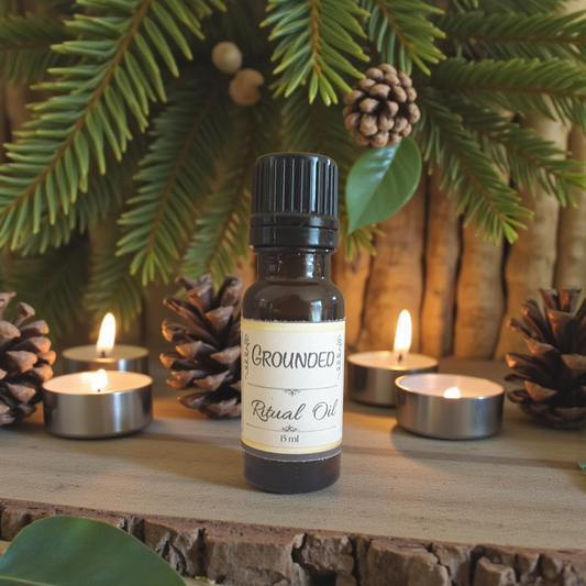 Bottle of 'Grounded' ritual oil with candles and pinecones on a wooden surface.