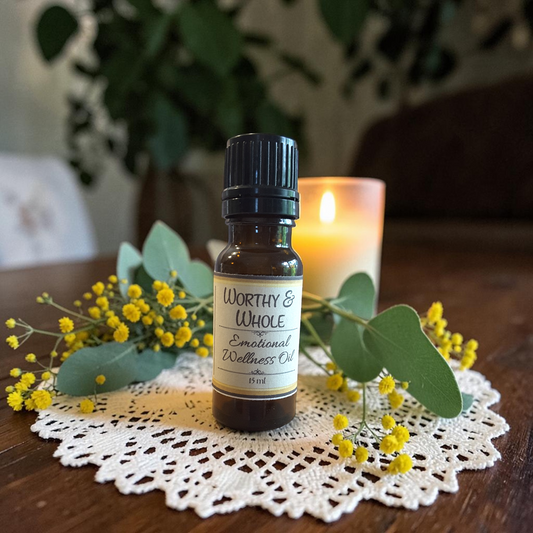 Worthy & Whole Emotional Wellness Oil on a doily on a wooden surface with yellow flowers and a candle in the background