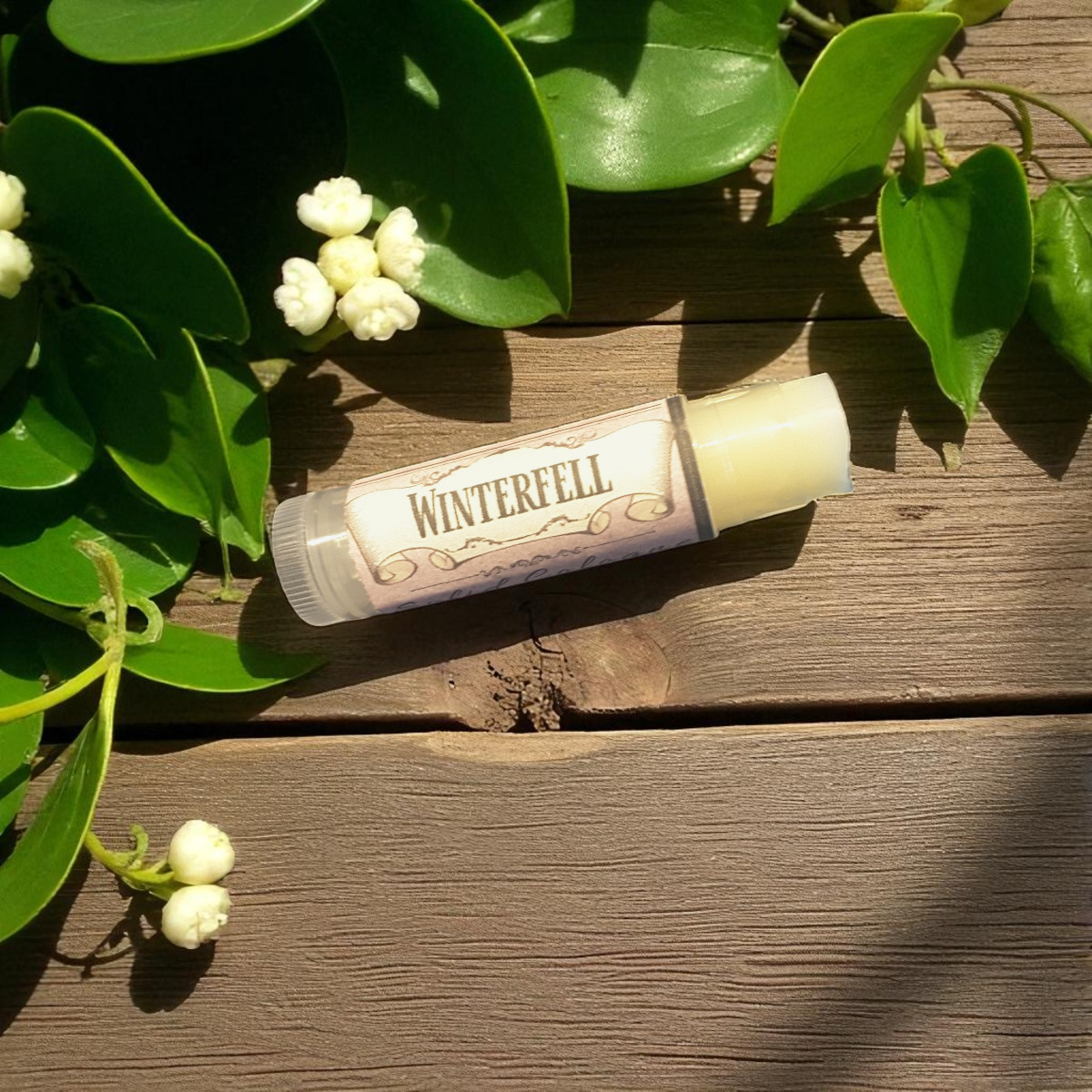 Winterfell solid cologne on a wooden surface with green leaves and flowers.