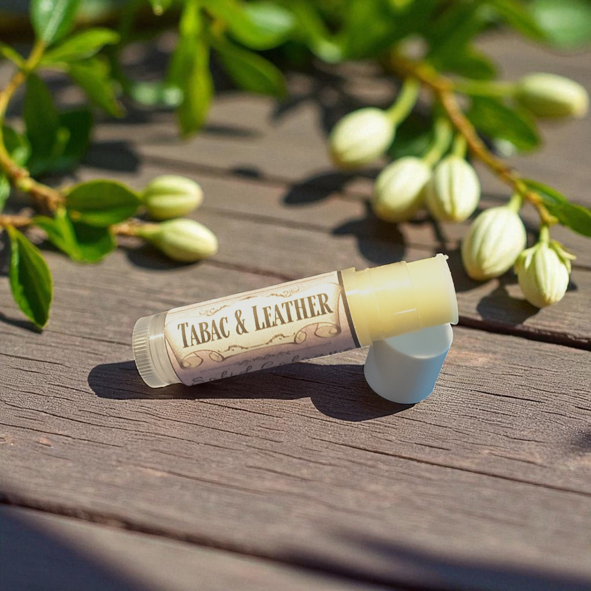 Tabac & Leather solid cologne on a wooden surface with green leaves in the background