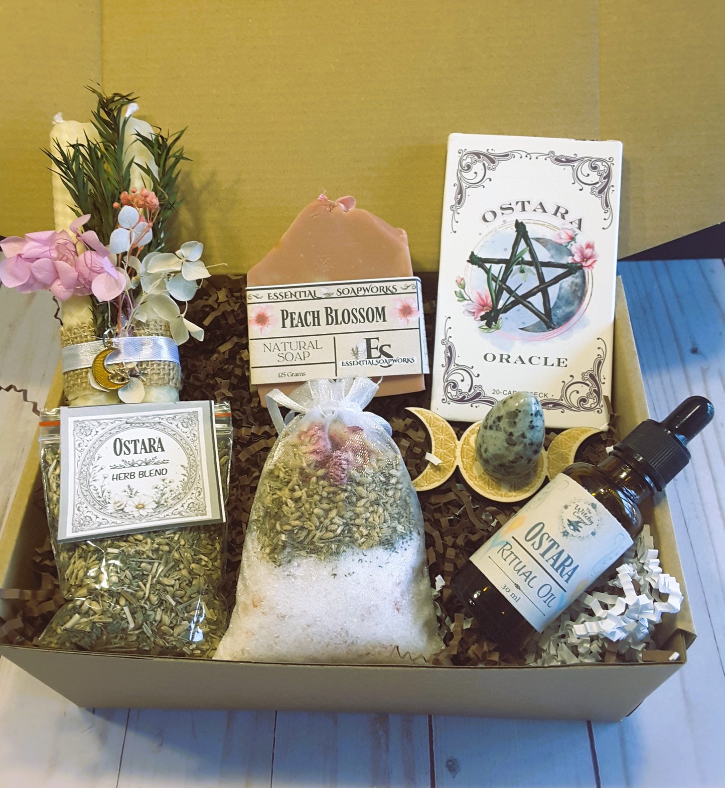 Collection of Ostara products including soap, oils, and herbs in a box on a wooden surface.