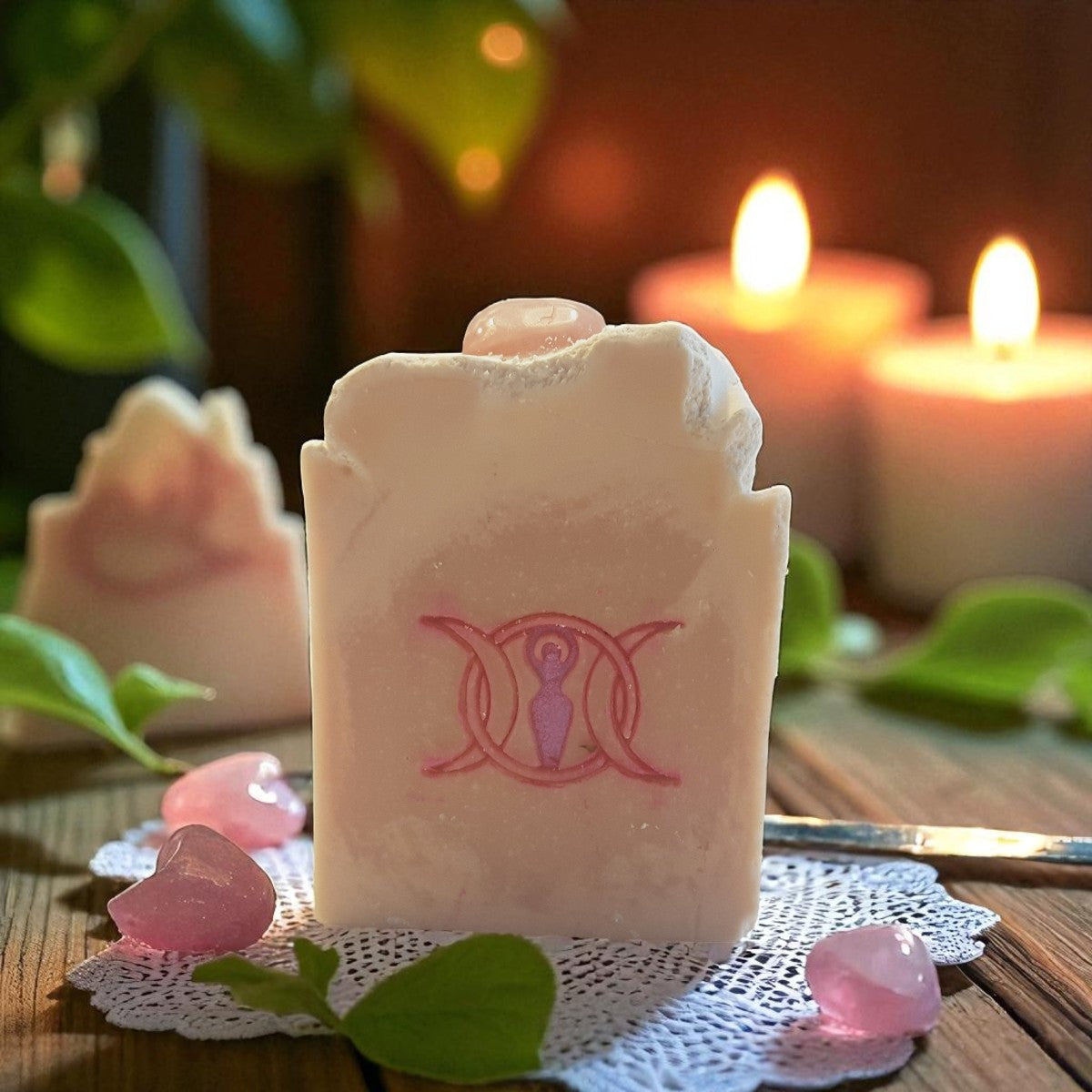 Rose quartz vegan crystal soap bar with a triple goddess symbol on a doily with candles and flowers in the background