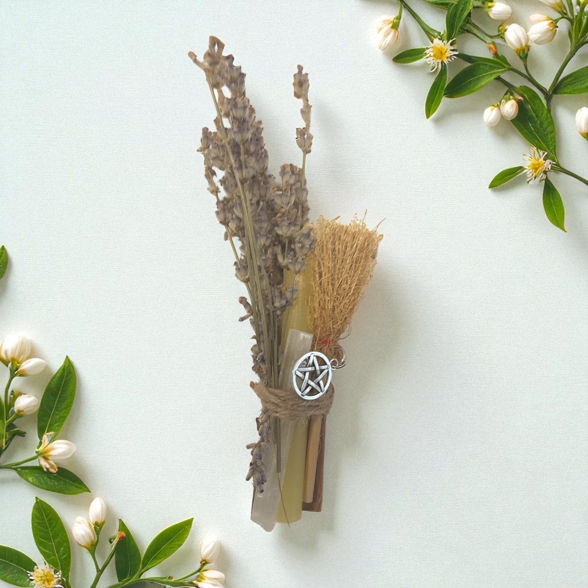 Decorative broom with pentacle charm surrounded by flowers on a light background