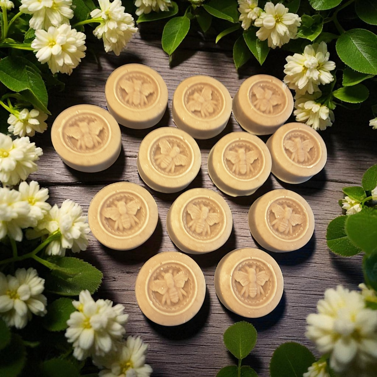 honey bee soap bars on a wooden surface surrounded by white flowers and green leaves.