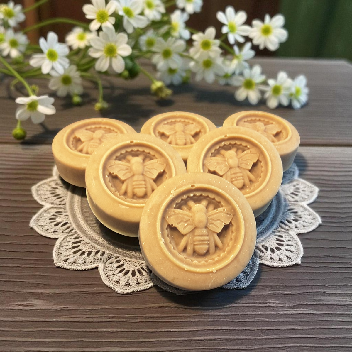 honey bee soaps with bee designs on a wooden surface with flowers in the background