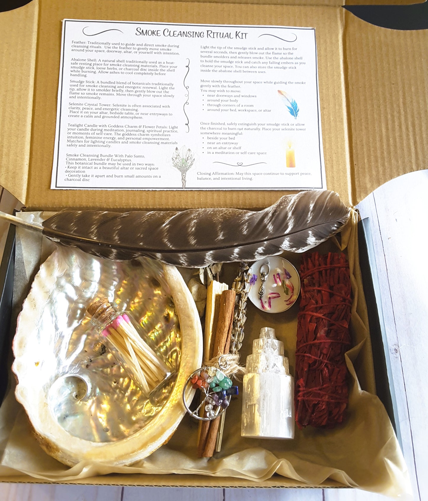 Smoke cleansing ritual kit featuring white sage and dragon’s blood smudge stick, abalone shell, selenite crystal tower, candle, and botanicals