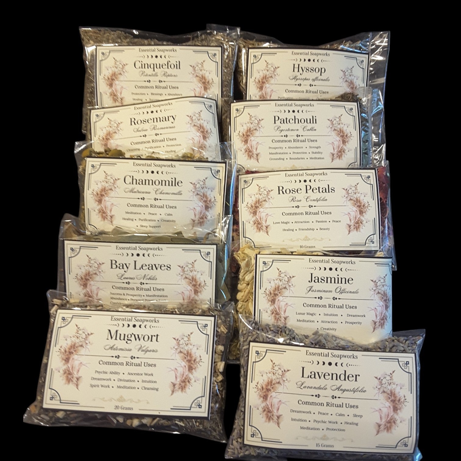 A set of ten individually packaged herbs for witchcraft arranged in a grid against a solid black background. Each clear plastic bag contains a single herb with a white paper label featuring elegant vintage-style typography and delicate floral illustrations.