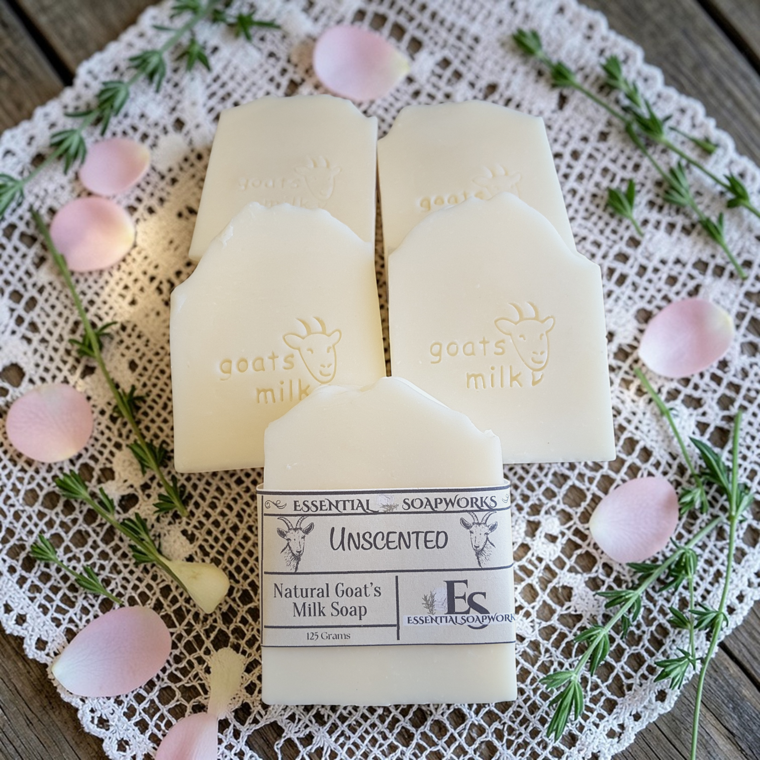 Three bars of Unscented Natural Goats' Milk Soap from Essential Soapworks on a lace doily with pink flowers and greenery.